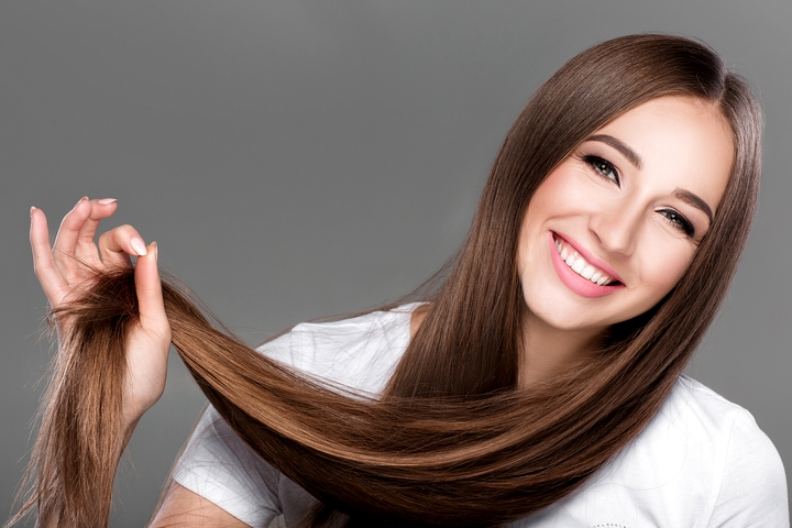 A woman with long brown hair is smiling after Hair regrowth treatment
