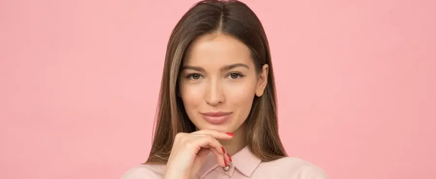 A young woman is posing during an Exilis Elite Treatment against a pink background.